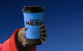 A cheerful Meerkat enjoying a cup of coffee and a pastry at Caffè Nero. Meerkat Rewards Savings